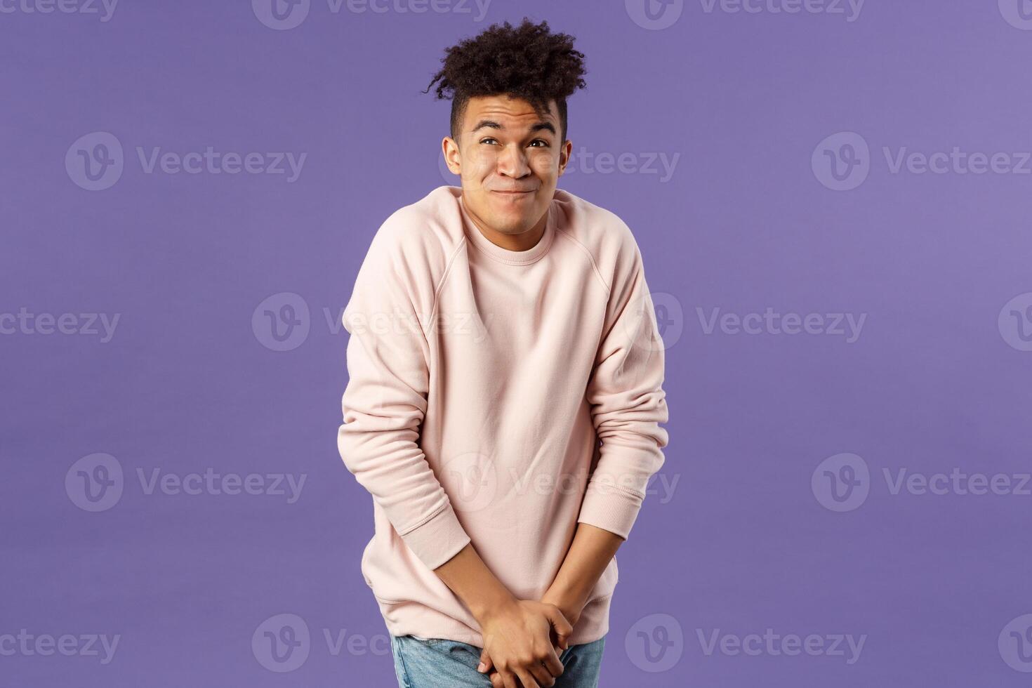 Portrait of young man need to pee, cant hold it looking at clock while standing in line, being in queue to toilet, drank too much water, standing with discomfort hold hands on pants photo