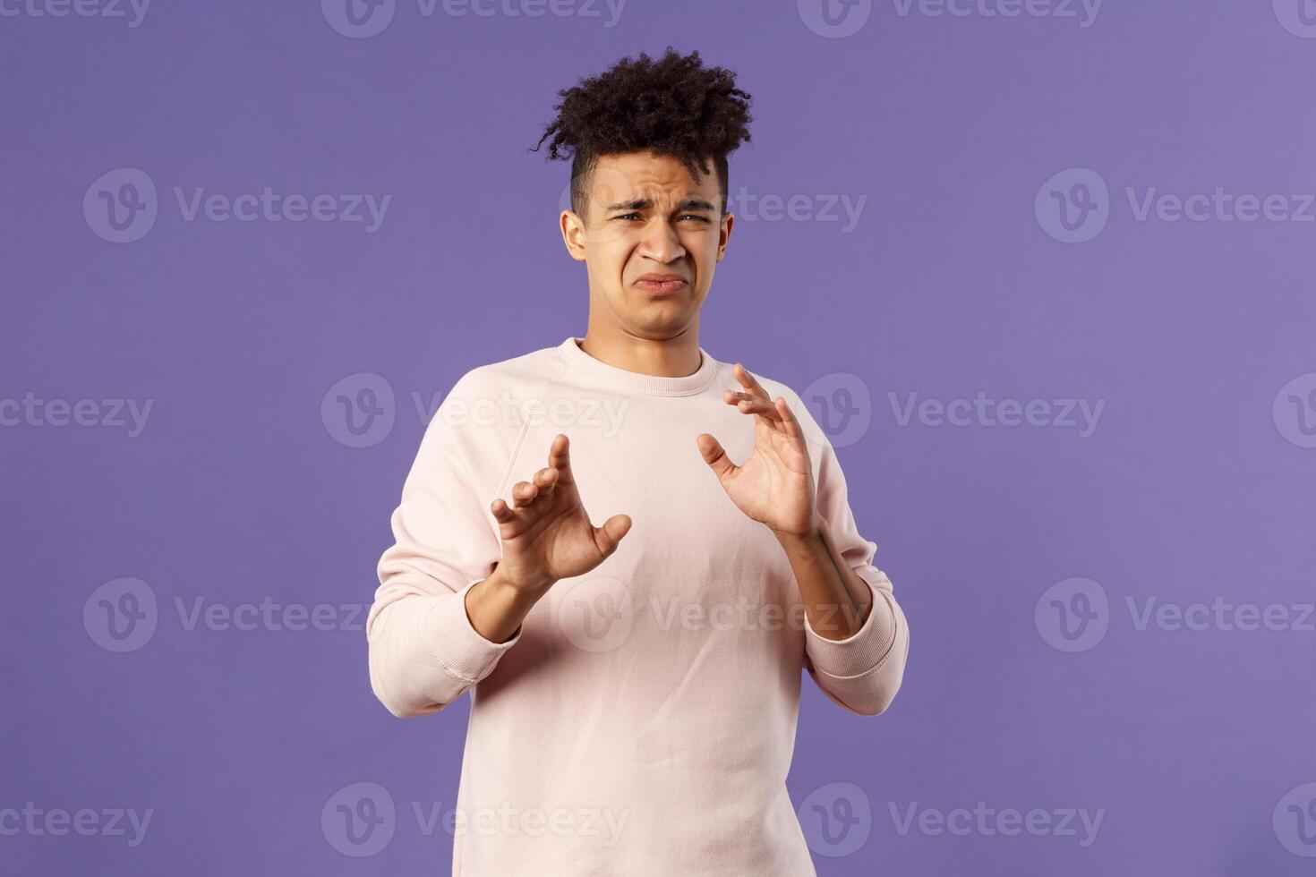 Phew get it away from me. Portrait of disgusted young man smelling something awful, step away and blocking it with raised arms, refuse grimacing with aversion and reluctance, purple background photo