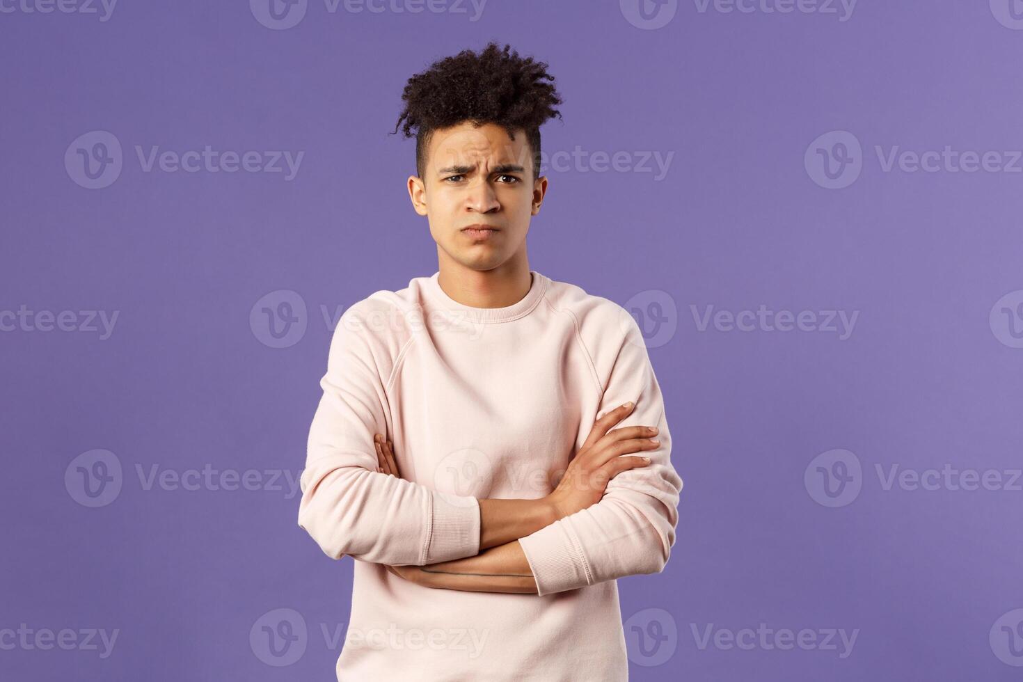 Portrait of young offended hispanic boyfriend, frowning and looking judgemental upset at camera, cross hands over chest defensive insulted pose, standing purple background angry at someone photo