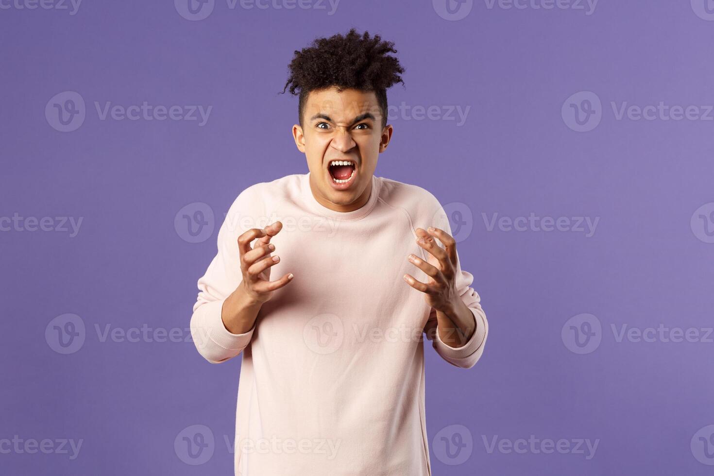 Portrait of hateful, outraged young hispanic man losing his temper, want to strangle or attack someone, cursing being aggressive, squeeze hands into fist from rage and hate, purple background photo