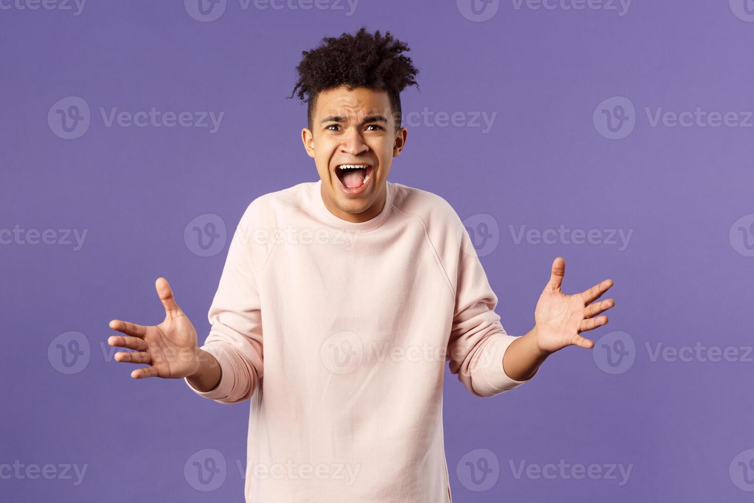 Portrait of concerned, upset and frustrated young man cant believe he lost, asking why, spread hands sideways in dismay, complaining shouting angry and uneasy, standing purple background photo