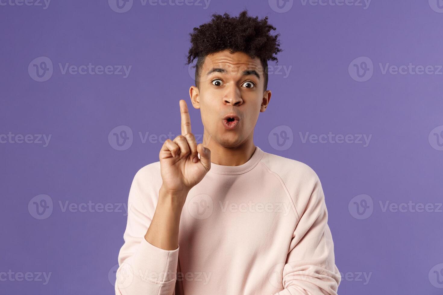 Got it, have plan. Portrait of excited happy young man, rejoicing as being striked with great idea, raise index finger in eureka gesture, figured out something, have suggestion, purple background photo
