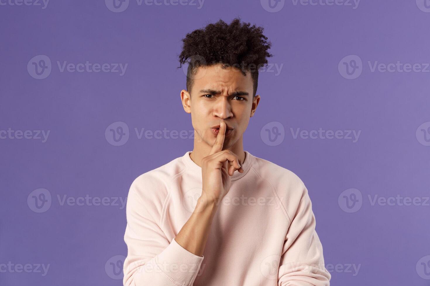 Show some respect. Portrait of angry and annoyed, displeased young hispanic man telling to keep quiet, shushing at someone being too loud, hold index finger over mouth frowning, scolding person photo