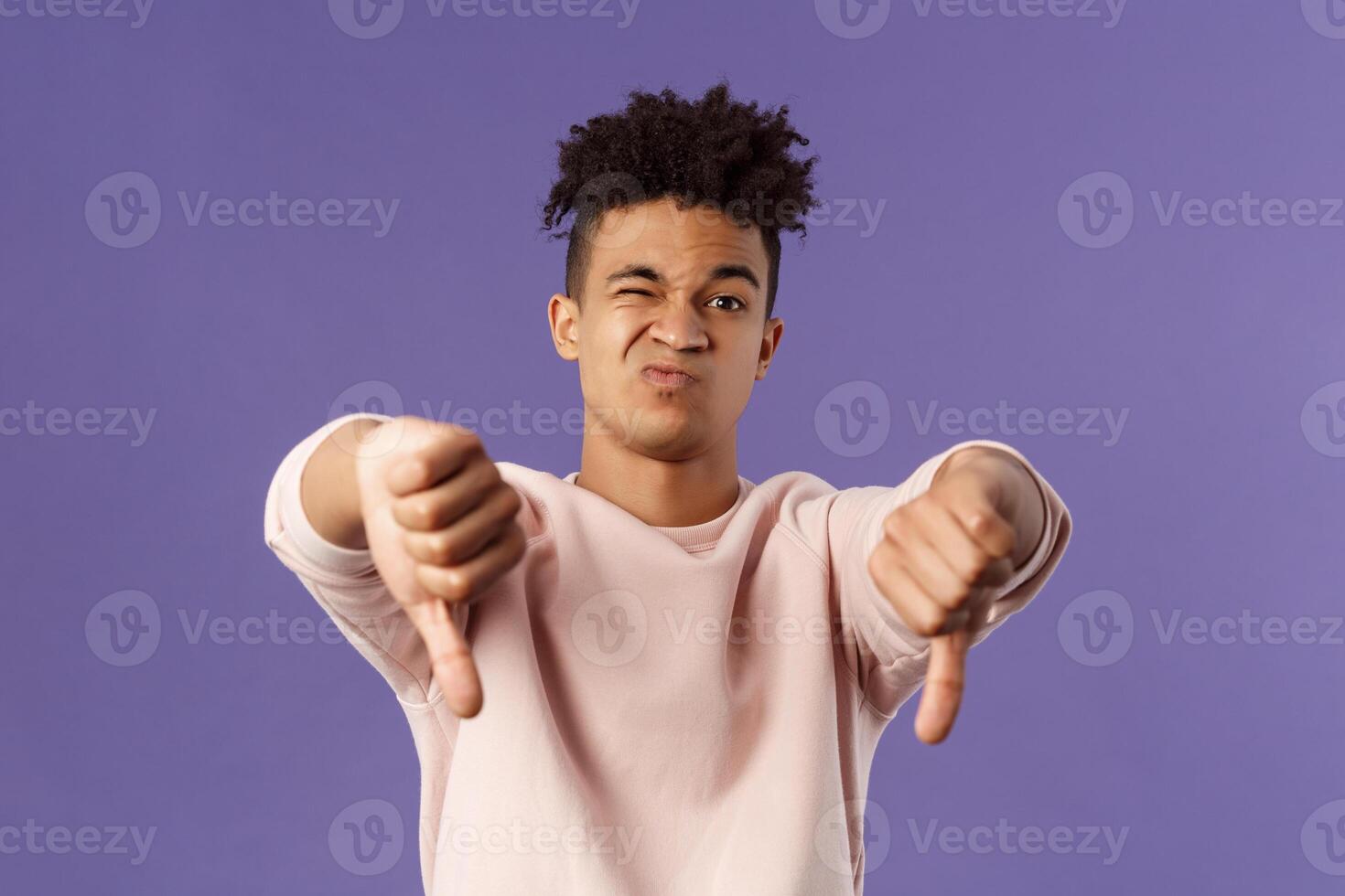 Close-up portrait of disappointed, unimpressed young hispanic man with dreads, grimacing skeptical, judging something bad, watched awful boring movie, show thumbs-down in dislike and disapproval photo