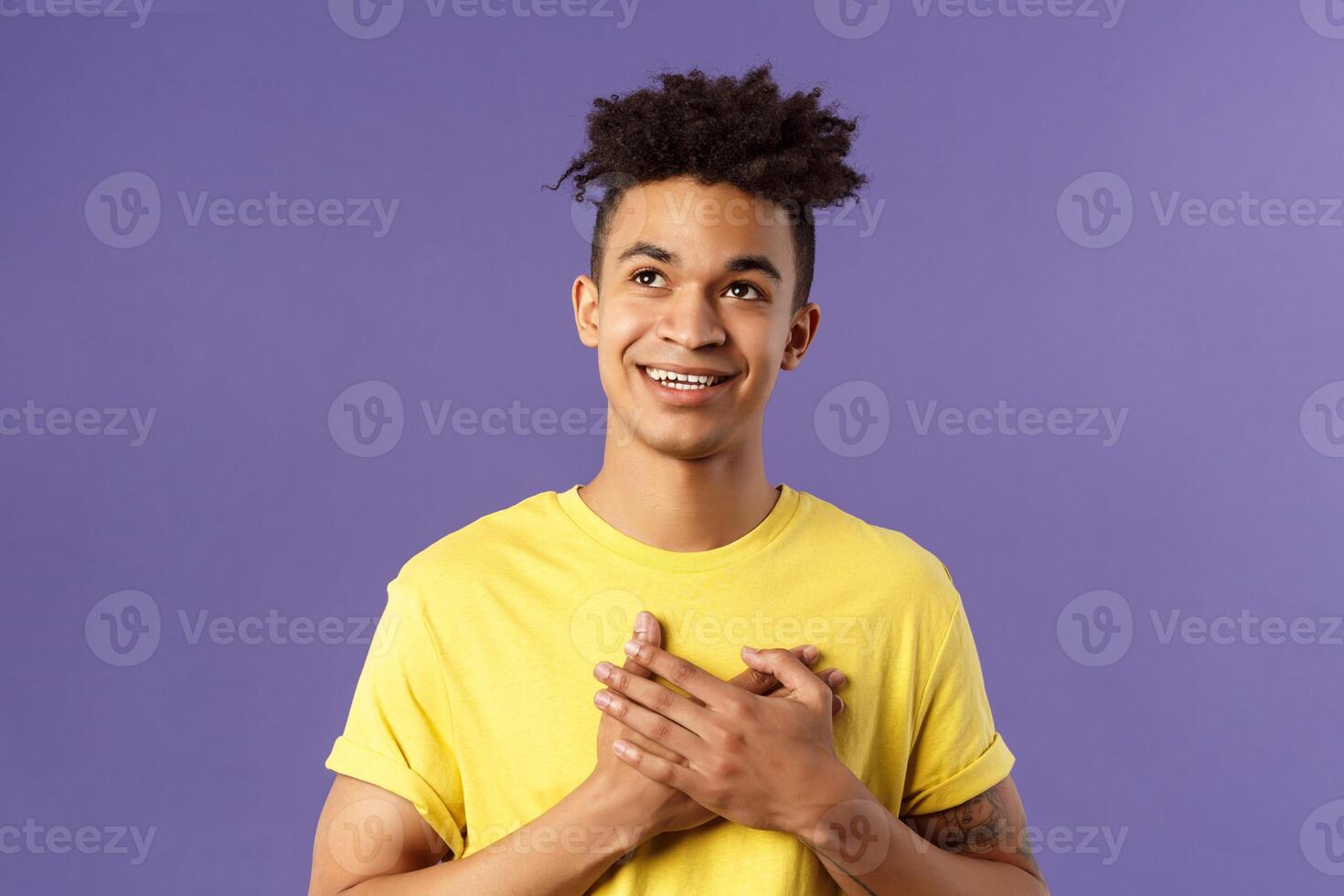 Close-up portrait of touched, romantic attractive man, hold hands on heart, remember nice lovely memory, looking up daydreaming, smiling pleased, appreciate something, purple background photo