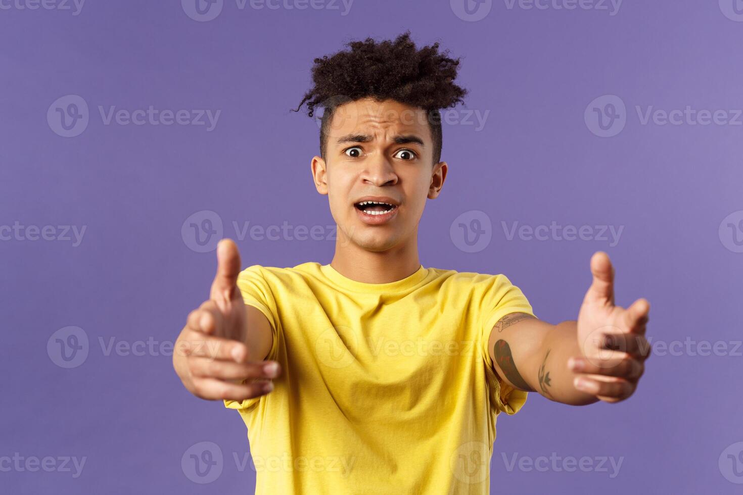 Waist-up portrait of concerned, nervous young man reaching hands forward to hold something but being scared, friend asking take baby for sec, standing very anxious and afraid, purple background photo