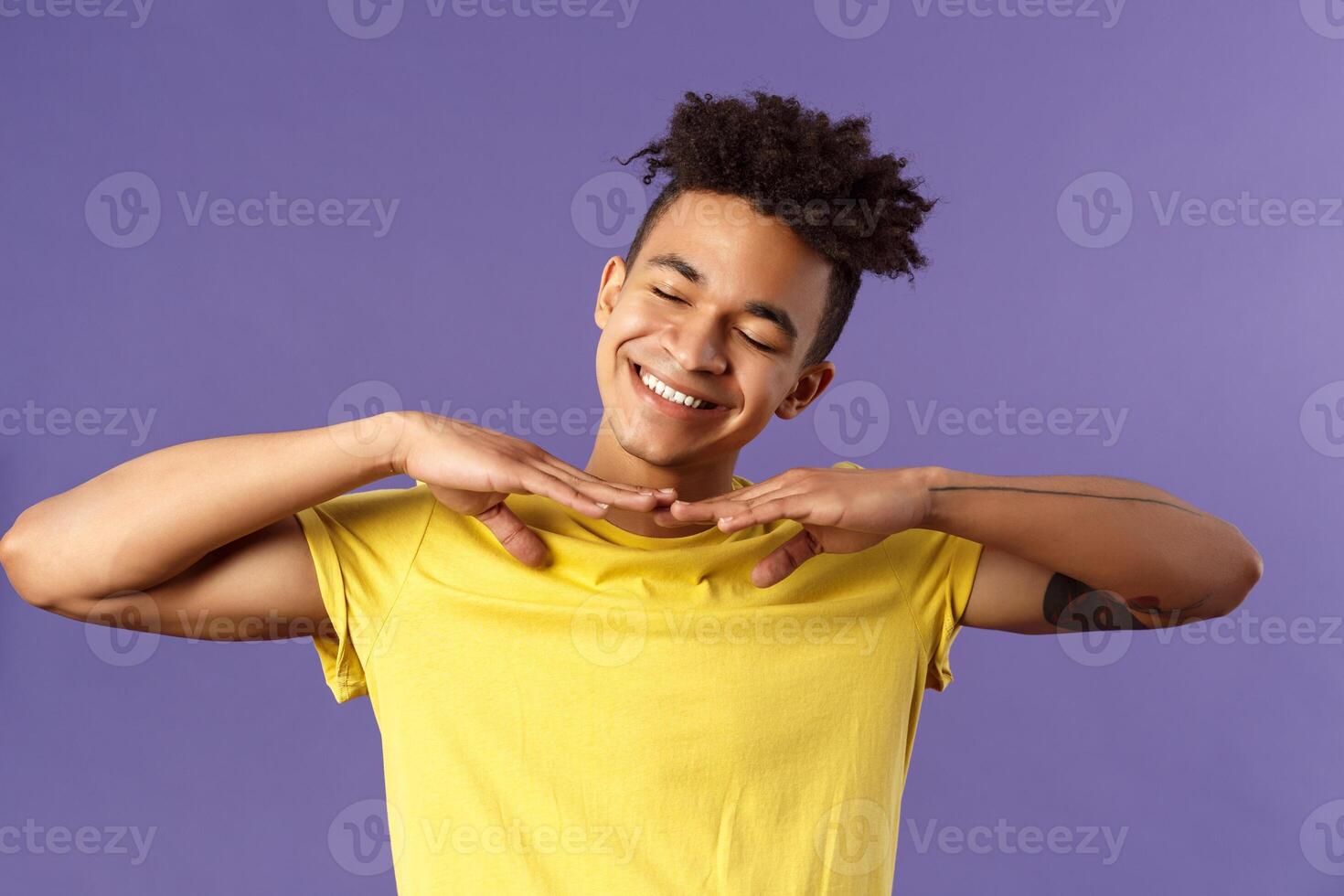 Close-up portrait of carefree handsome young man, do stretching exercises at home while on quarantine, hold hands sideways close eyes and tilt head dreamy, just woke up, purple background photo