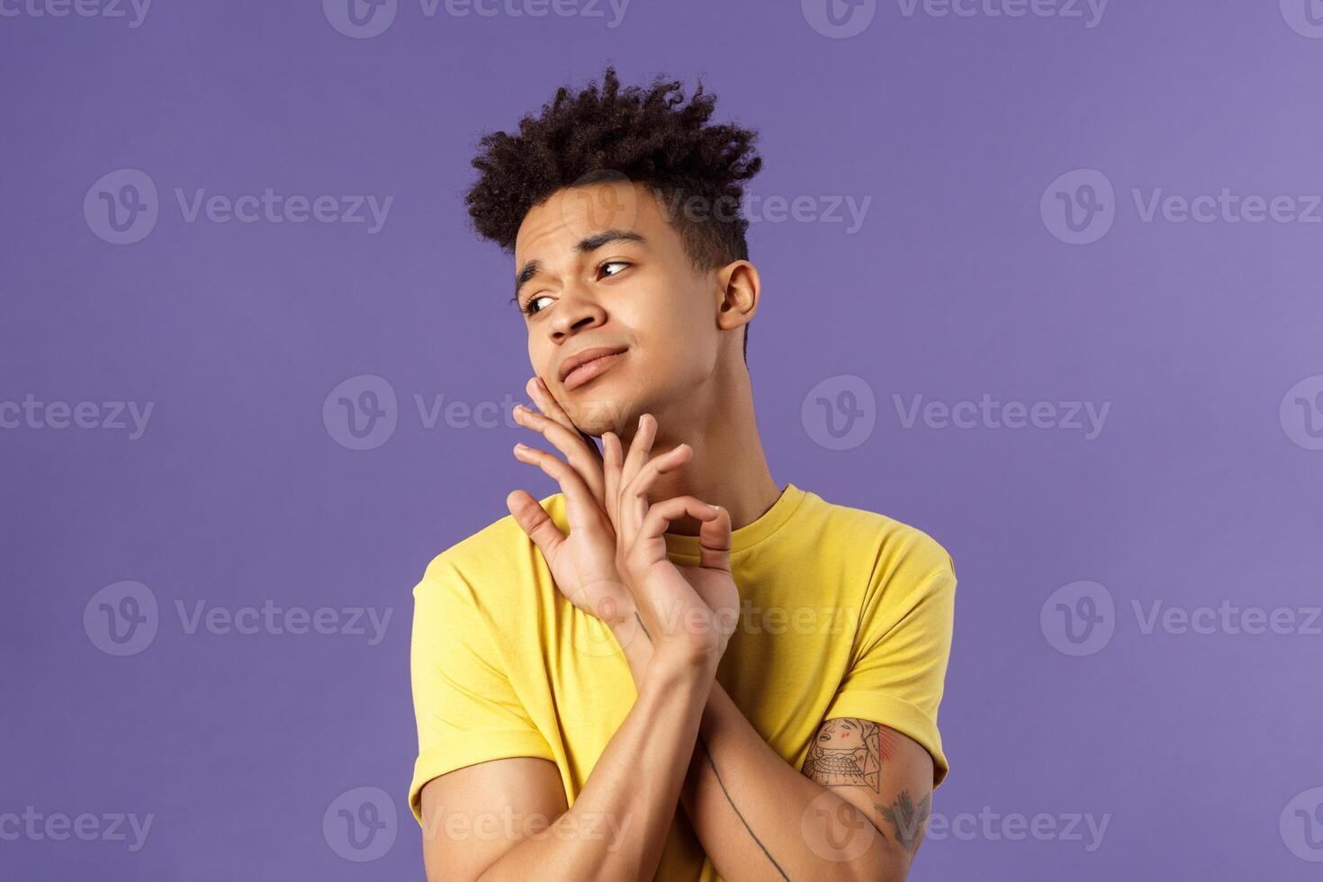 Close-up portrait of glamour beautiful young queer guy with dreads, standing in feminine model pose, gently touching face and looking away sensual, standing purple background photo