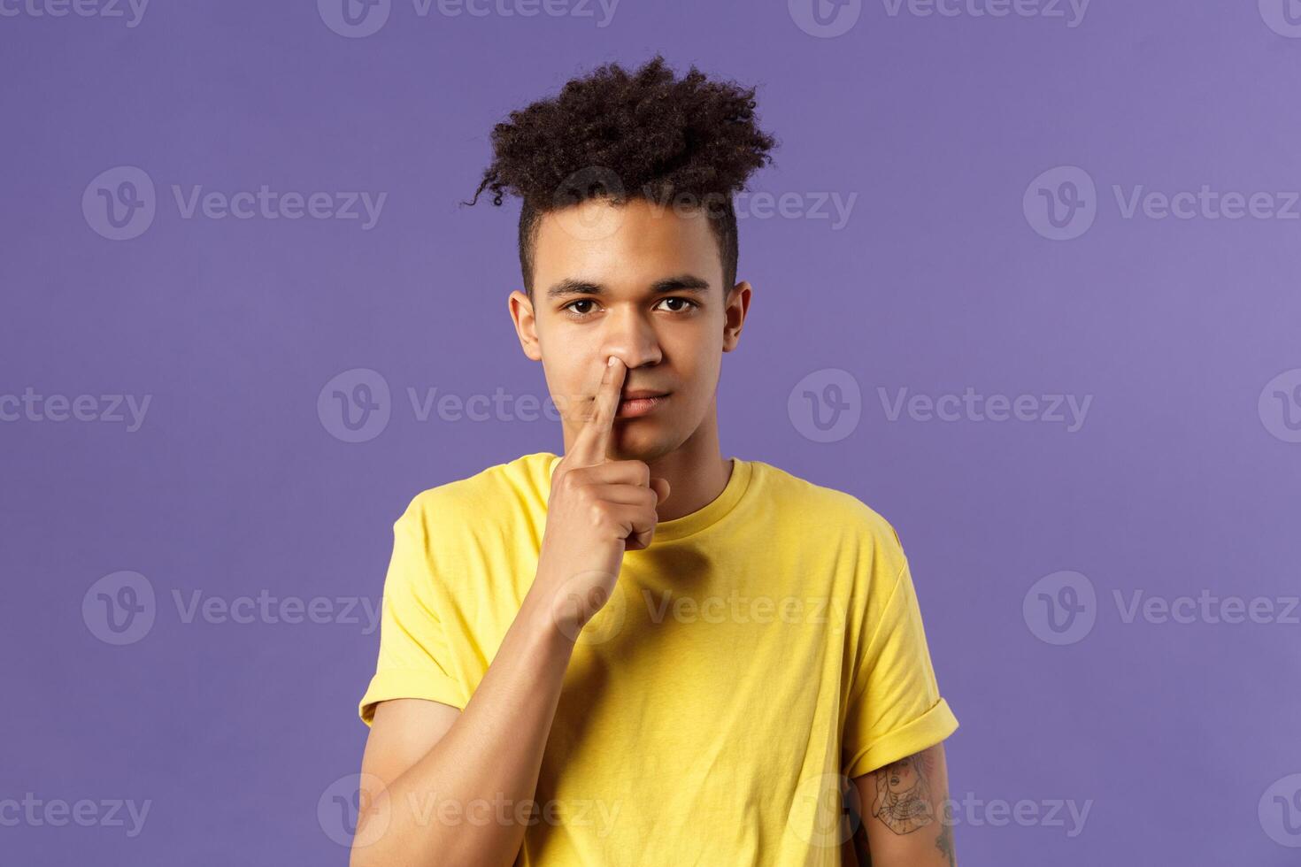 Close-up portrait of funny and unappropriate young hispanic teenage guy picking nose with finger, smiling and looking at camera, standing purple background, have bad habit photo