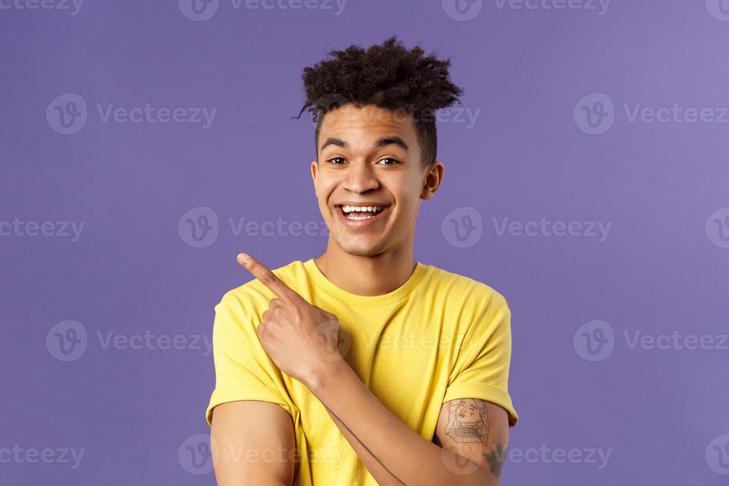 Close-up portrait of cheerful, attractive young male student showing promo, pointing at upper left corner, smiling pleased, recommend click link, visit page or download app, purple background photo