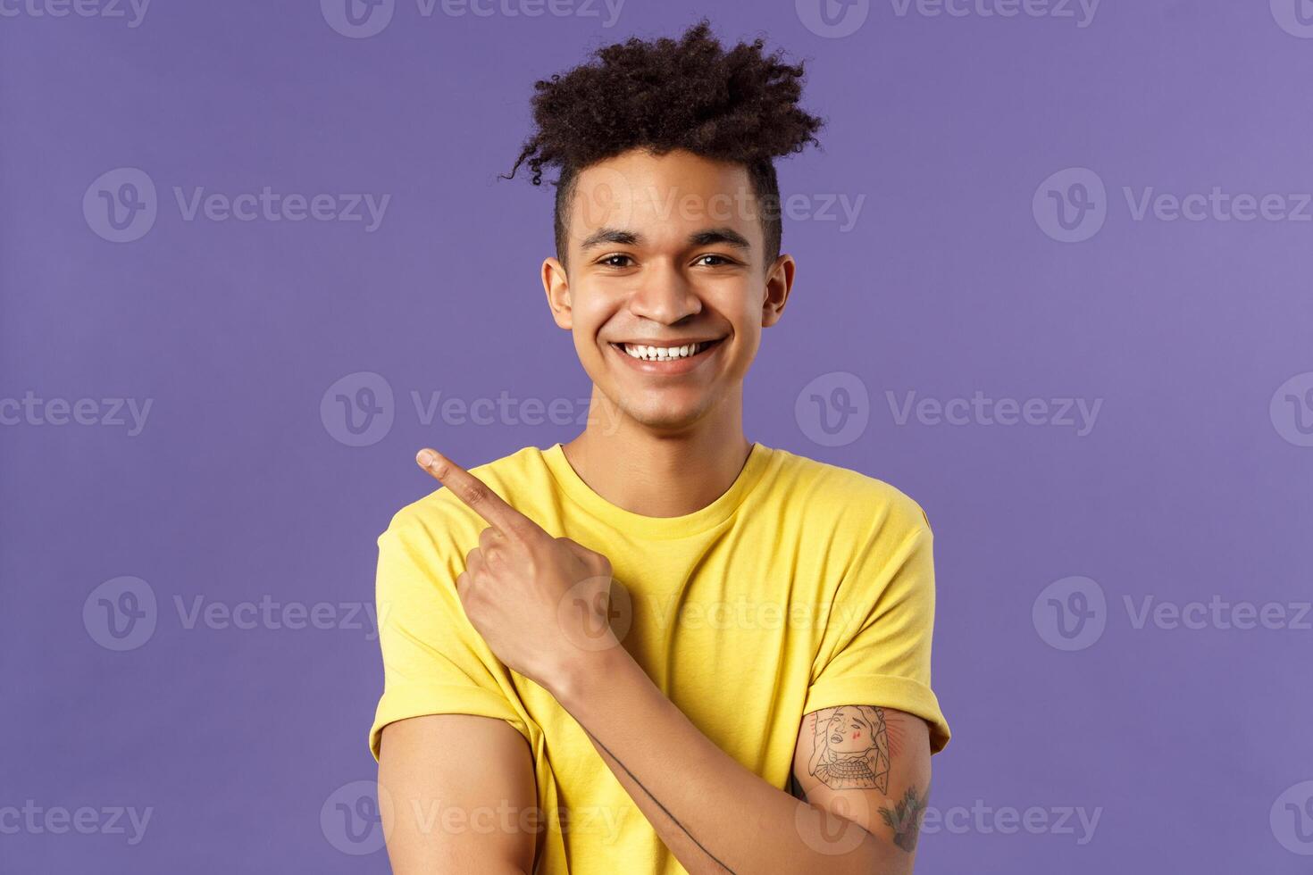 Close-up portrait of enthusiastic, happy young hipster male with dreads, beaming smile and pointing finger upper left corner, present cool product, introduce something really good, purple background photo