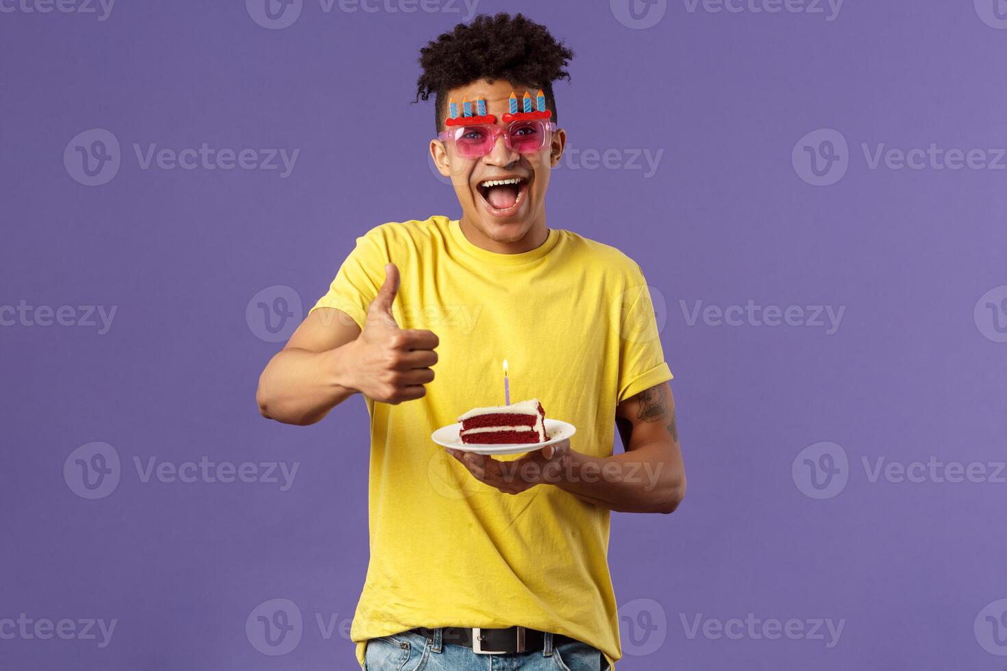 Celebration, party and holidays concept. Portrait of upbeat, cheerful young happy man celebrating birthday, wear funny sunglasses and hold b-day cake with lit candle, show thumb-up, recommend photo