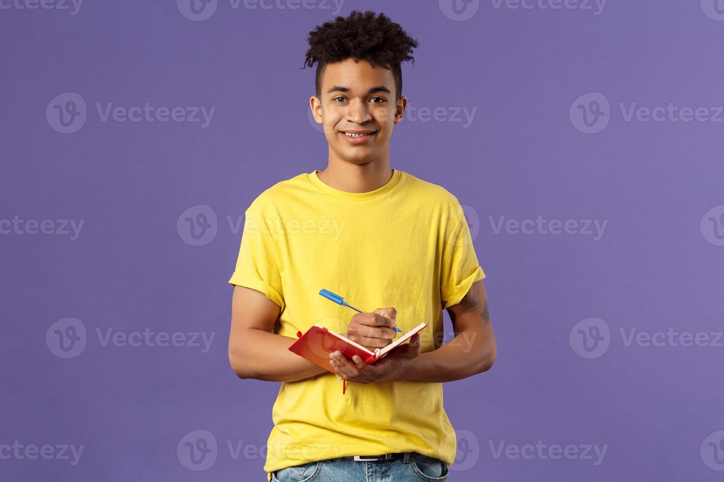 Portrait of young hispanic male student studying online courses, writing down lecture, making personal schedule or taking notes in planner, look camera enthusiastic and interested, purple background. photo