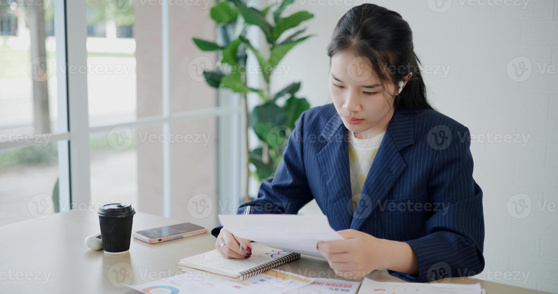 High angle view, Asian businesswoman in suit sits on table while analyze documents and taking notes in small coffee shop. Work from anywhere, Remote working photo
