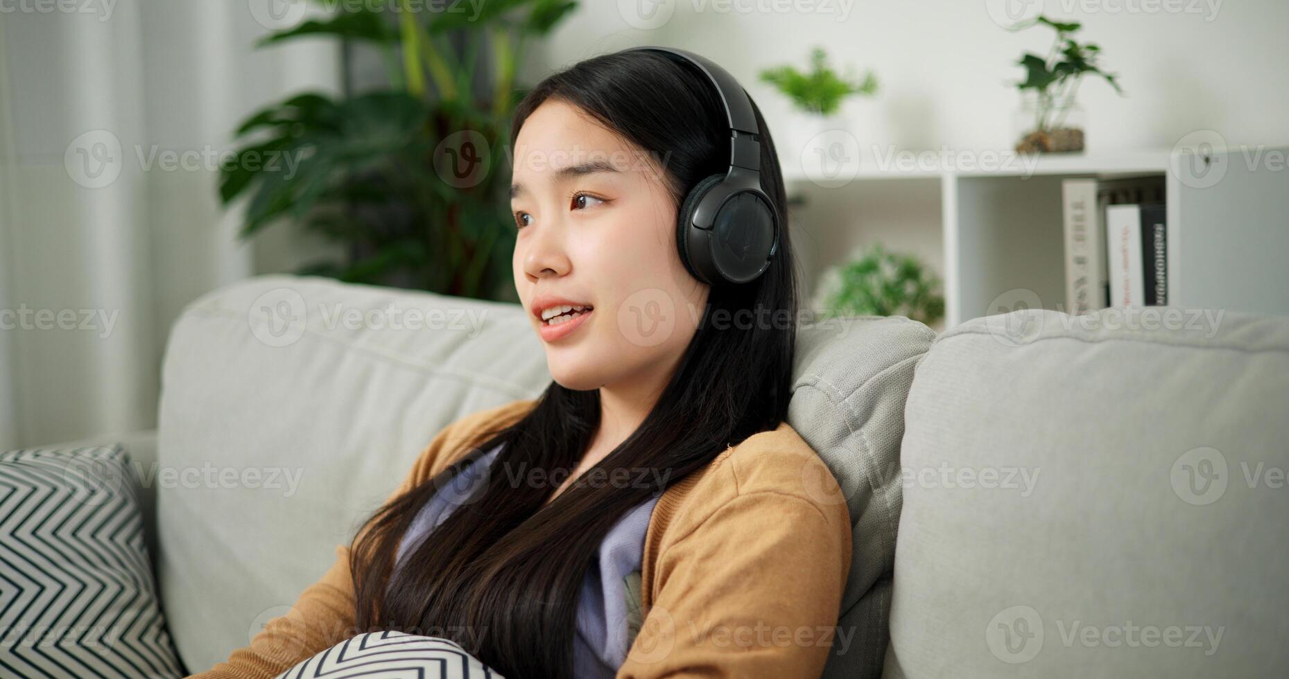 Portrait of Relaxed young Asian woman wear wireless headphones listen to music while sitting on the sofa in the living room at morning ,Free time photo