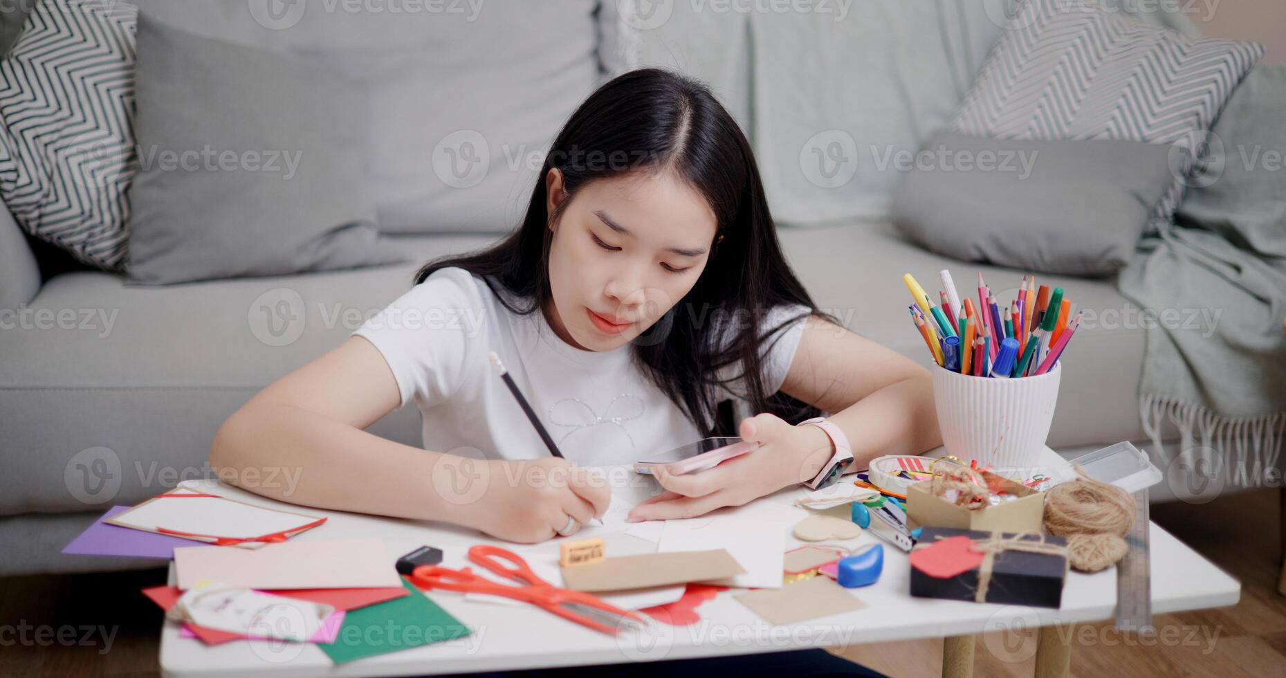 Portrait of Young Asian woman sitting on the floor uses a mobile phone to search for ideas for greeting cards. Holiday hobbies, crafts, DIY cards photo