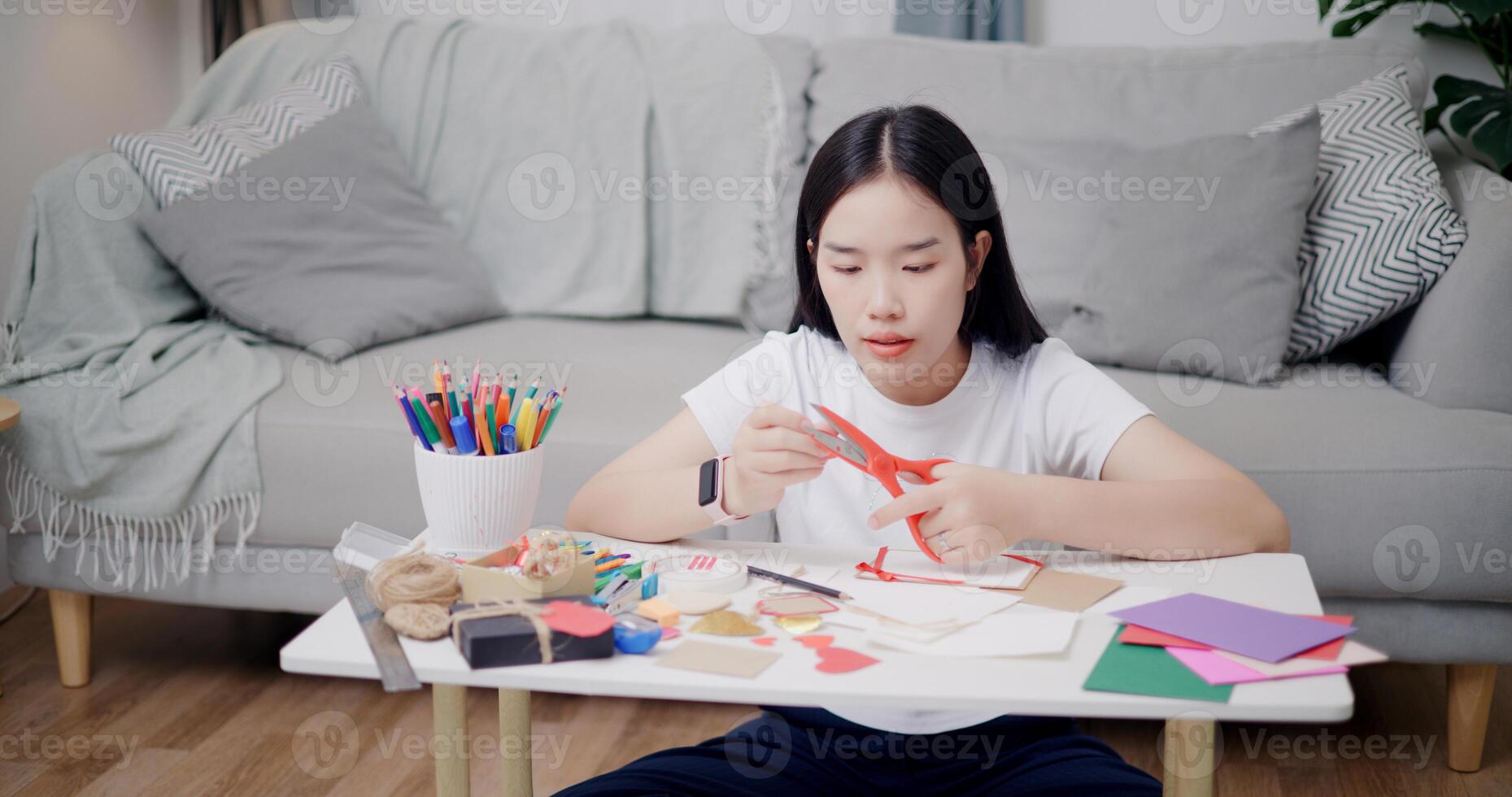Portrait of Young Asian woman sitting on the floor use scissors to cut paper hearts into stickers to make greeting cards. Holiday hobbies, Handmade, DIY card photo