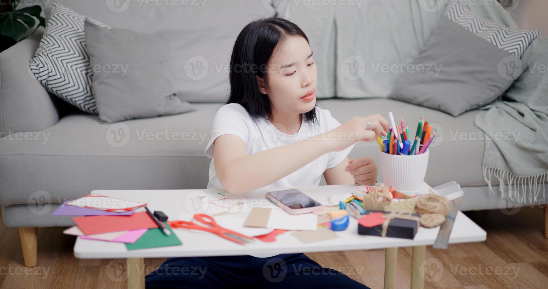 High angle view, Young Asian woman sitting on the floor uses a mobile phone to search for ideas for greeting cards. Holiday hobbies, crafts, DIY cards photo