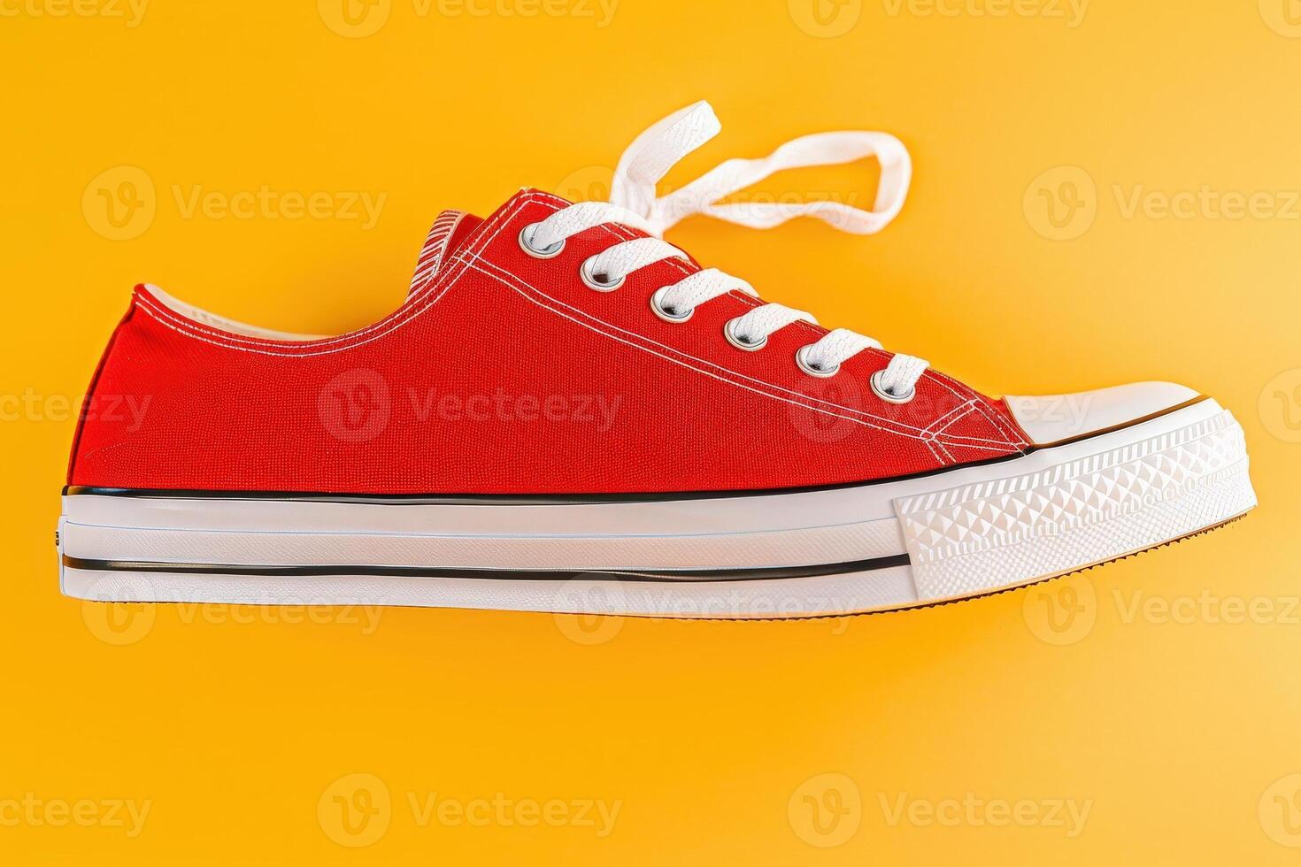 A striking pair of red sneakers rests on a sunny yellow backdrop, showcasing their design and color vibrancy in a lively composition. photo