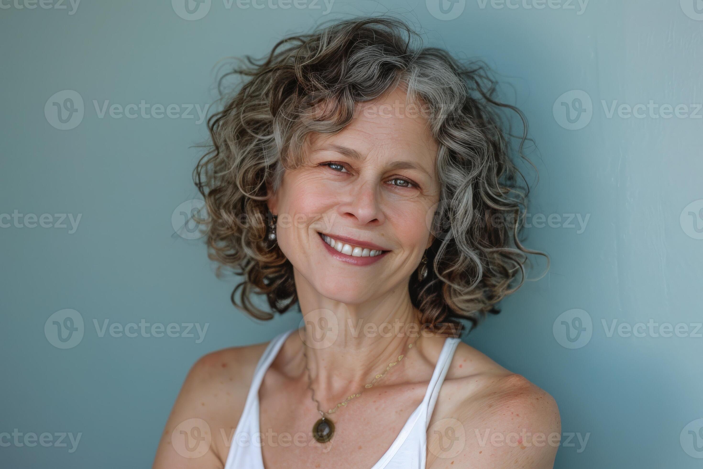 A joyful woman showcases her curly grey hair and bright smile, creating