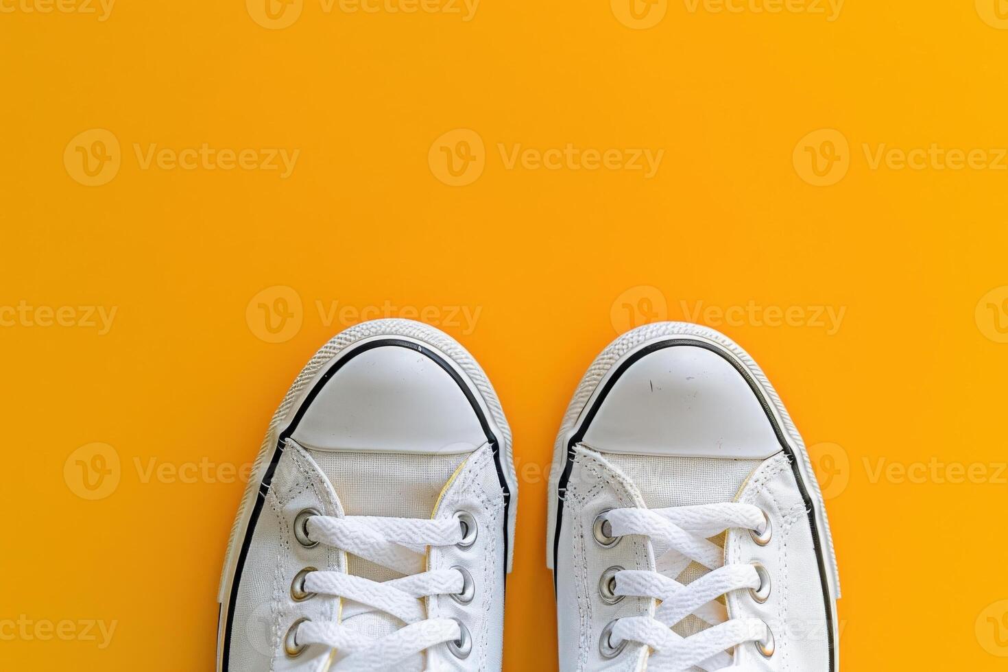 A pair of pristine white sneakers lies isolated on a vibrant yellow backdrop, showcasing their modern design and versatility. photo