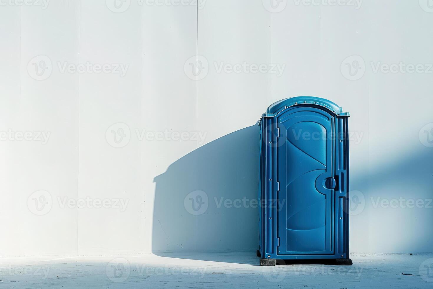 A sleek blue portable restroom stands alone against a stark white wall, casting a long shadow in the warm sunlight. photo
