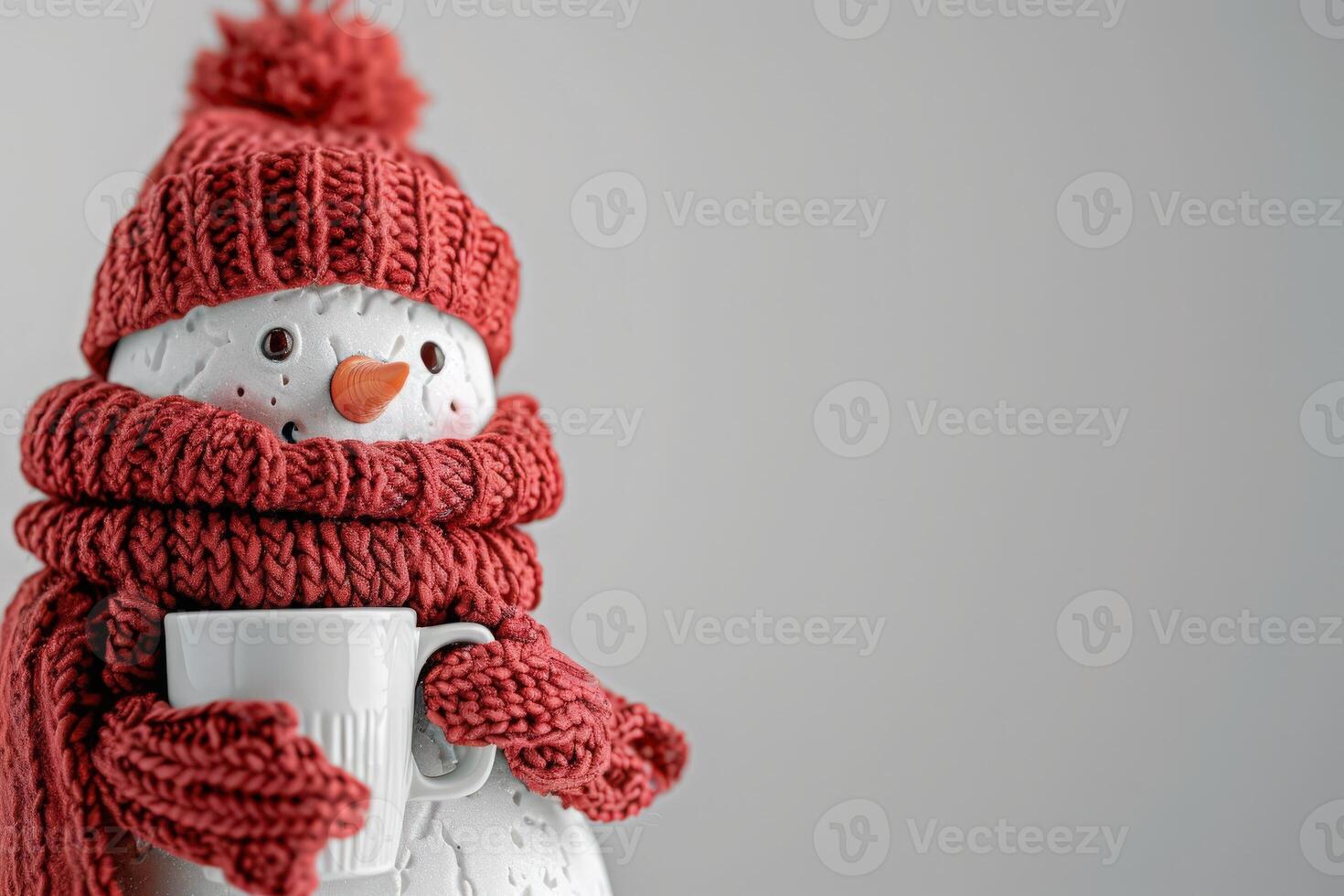 A delightful snowman figurine, wrapped in a red knitted scarf and hat, holds a white cup, evoking winter warmth and joy. photo