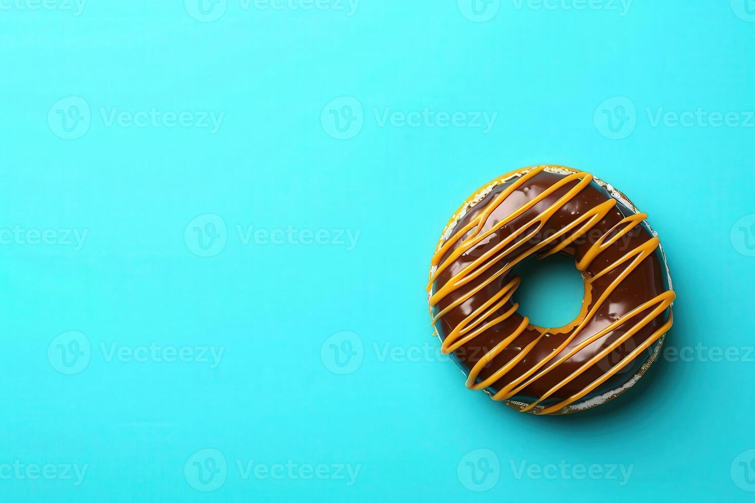 A mouthwatering chocolate covered donut sits against a vibrant turquoise backdrop, adorned with a tempting golden drizzle. photo
