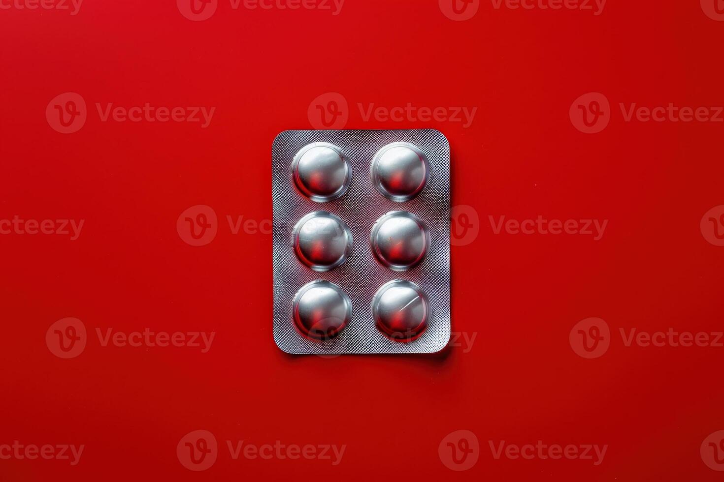 A blister pack containing six shiny white pills rests against a vibrant red backdrop, creating a striking contrast that draws attention. photo