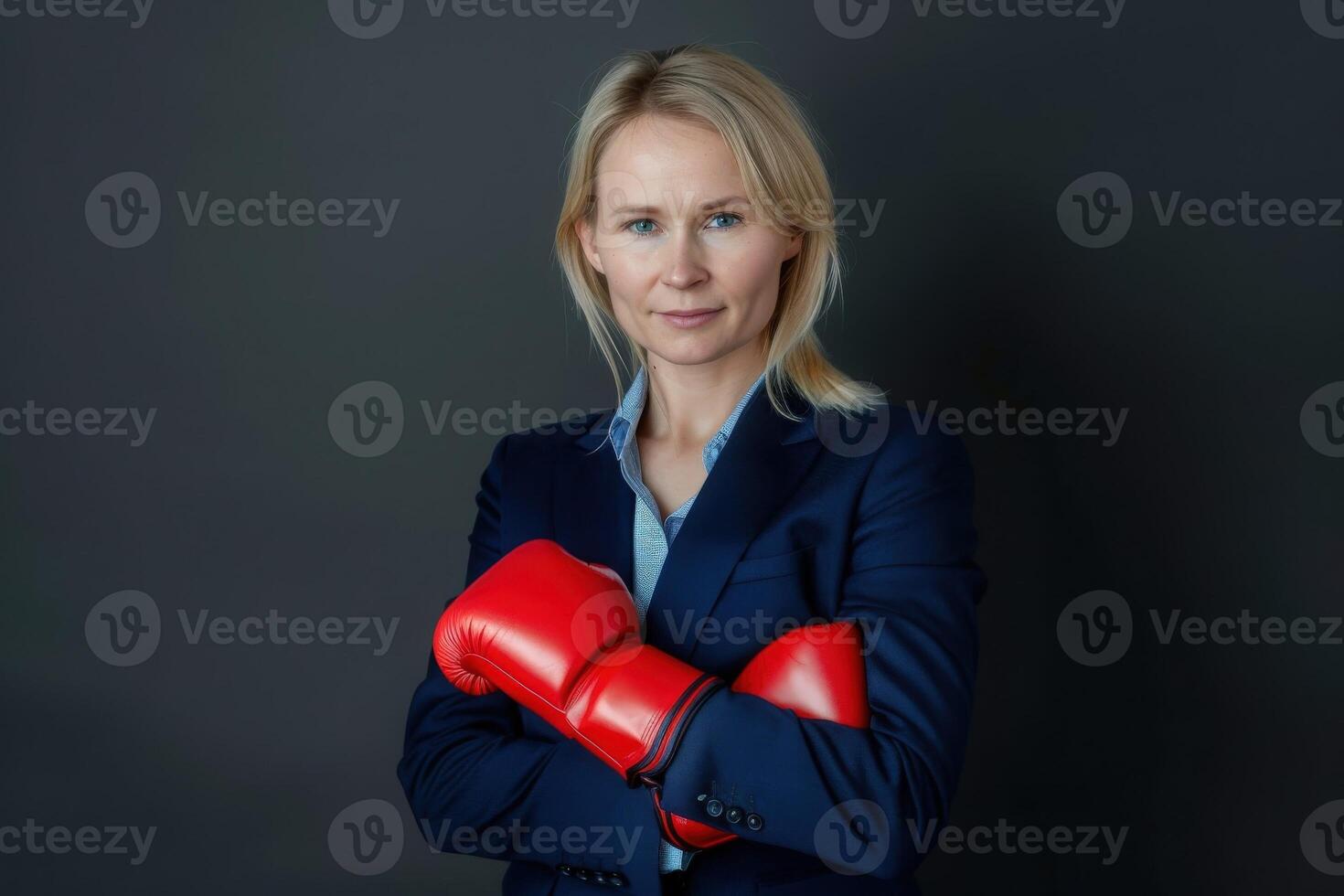 A confident woman in a tailored suit stands with her arms crossed, showcasing her vibrant red boxing gloves and determination. photo