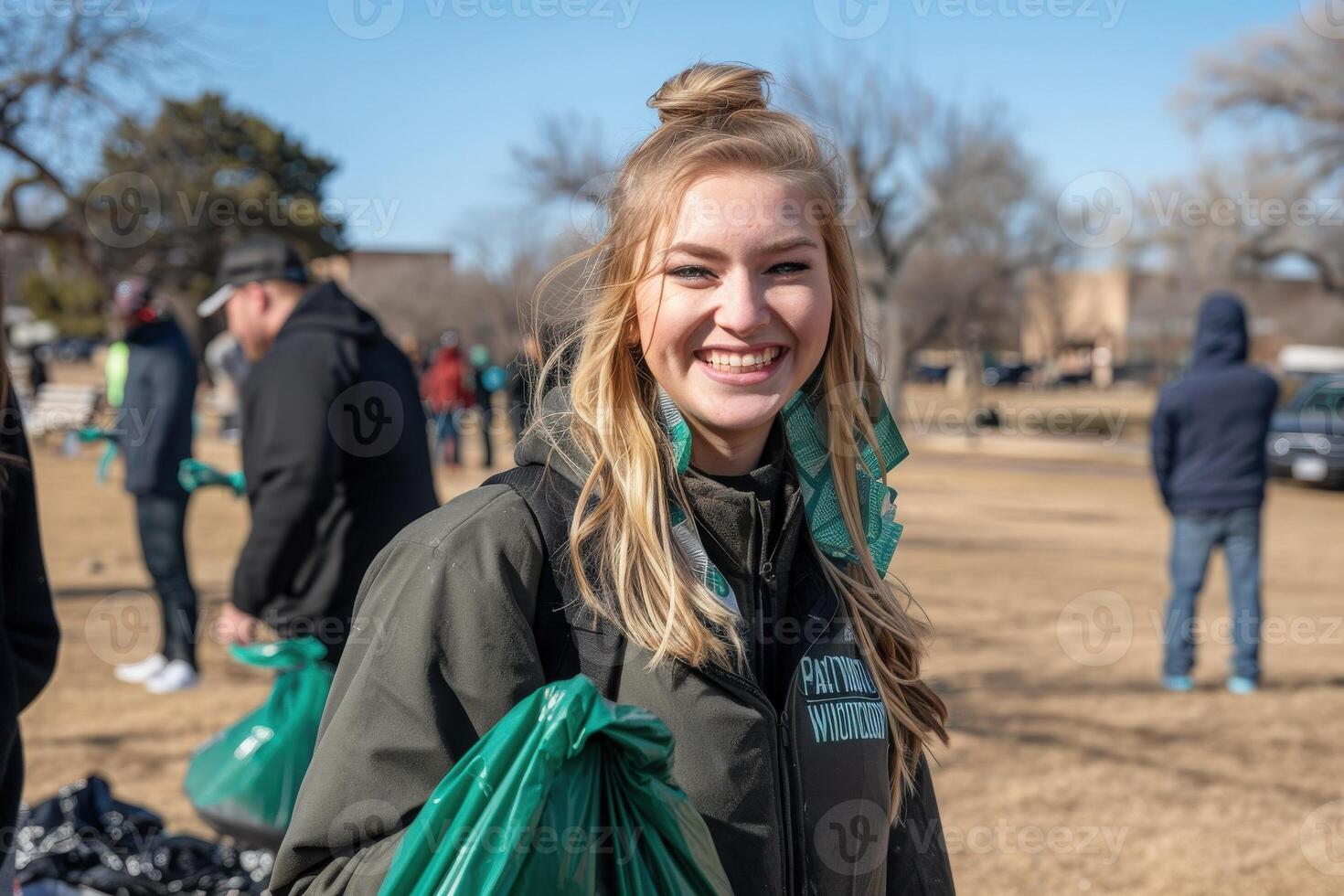 A young volunteer with a bright smile actively participates in a park cleanup, holding a green trash bag under the clear blue sky. photo