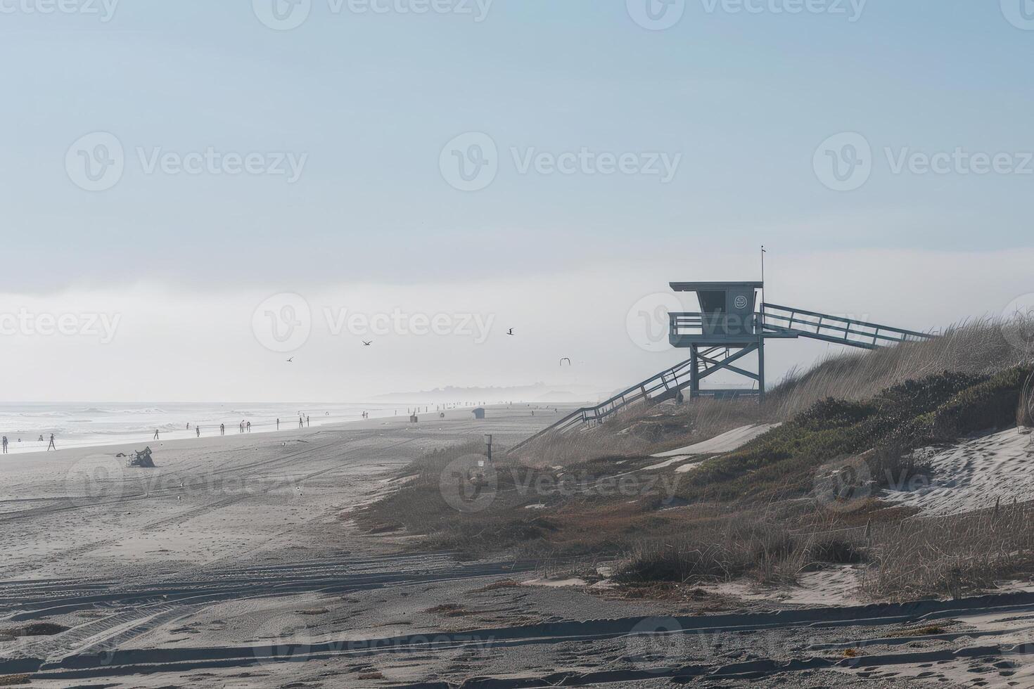 A lone lifeguard tower stands on a sandy beach, overlooking a misty ocean. A few people are scattered along the shore, enjoying a sunny day. photo