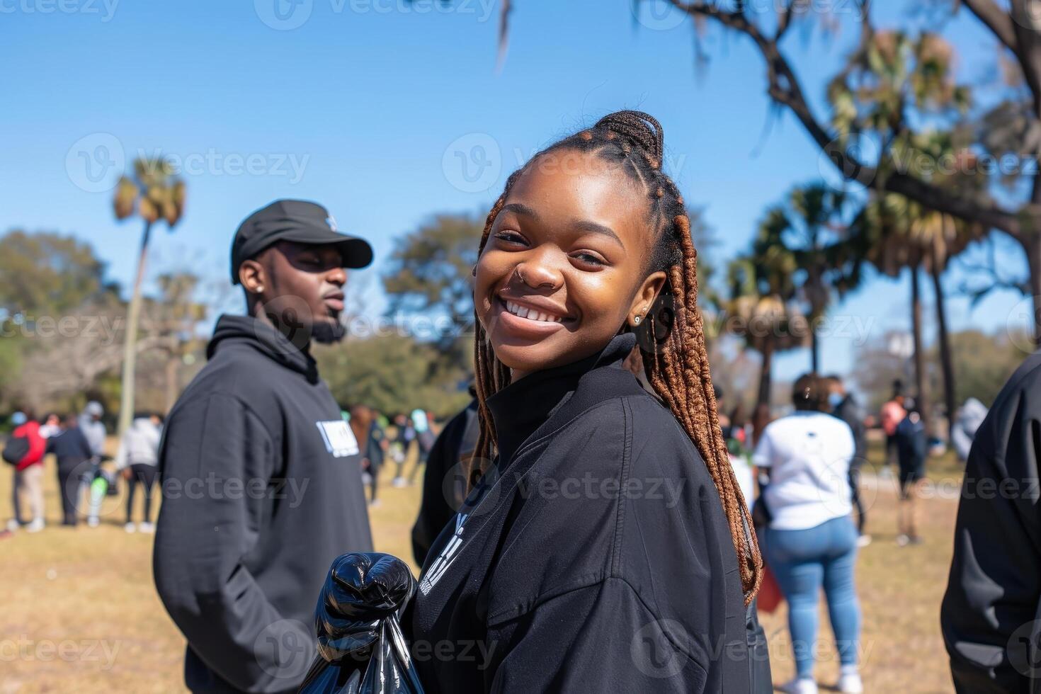 A young volunteer beams with joy while holding a bag, surrounded by fellow helpers at a sunny community cleanup day. photo
