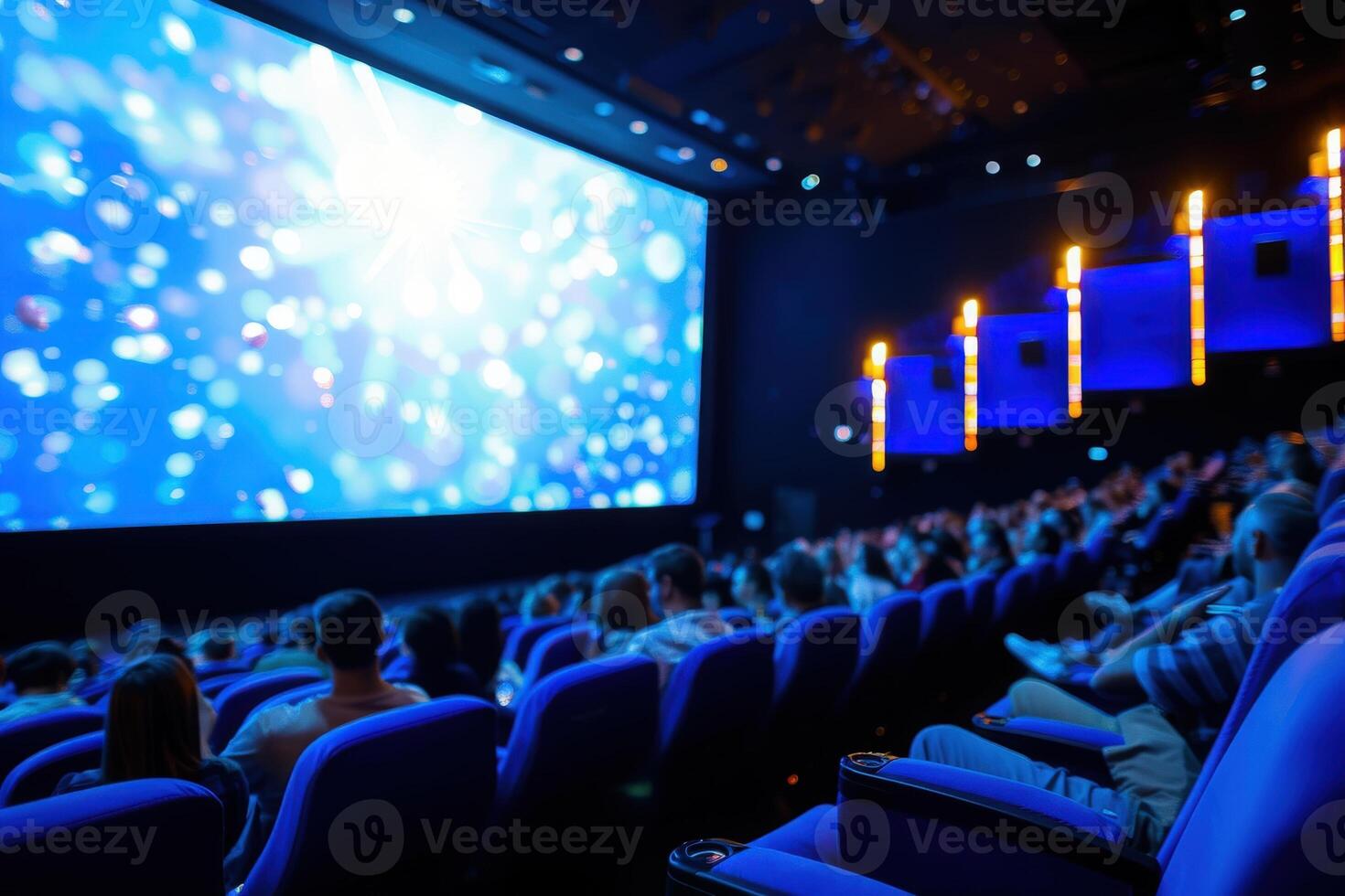 A captivated audience fills the plush seating of a dimly lit theater, immersed in a mesmerizing performance projected on a large screen. photo
