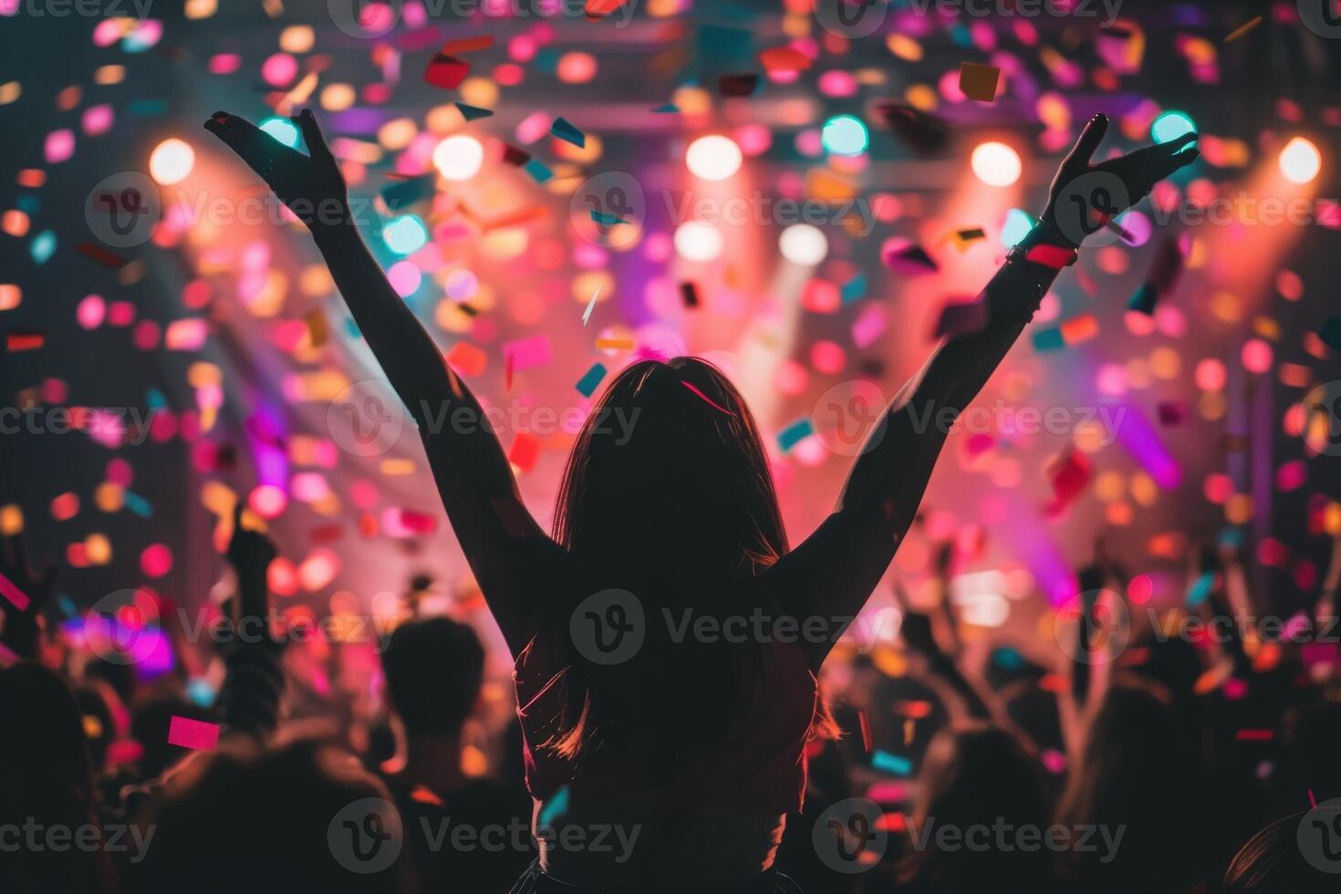 Amidst a lively crowd, a woman joyfully raises her arms while colorful confetti flutters down, celebrating the festive atmosphere of the night. photo