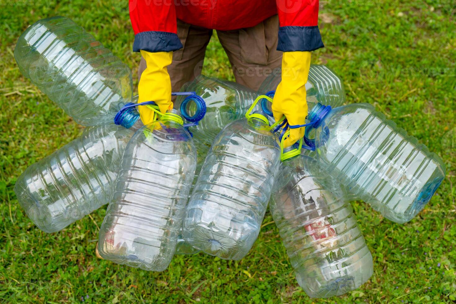 Garbage collection. Hands in yellow gloves holding big empty plastic bottles. Grass on a background. photo