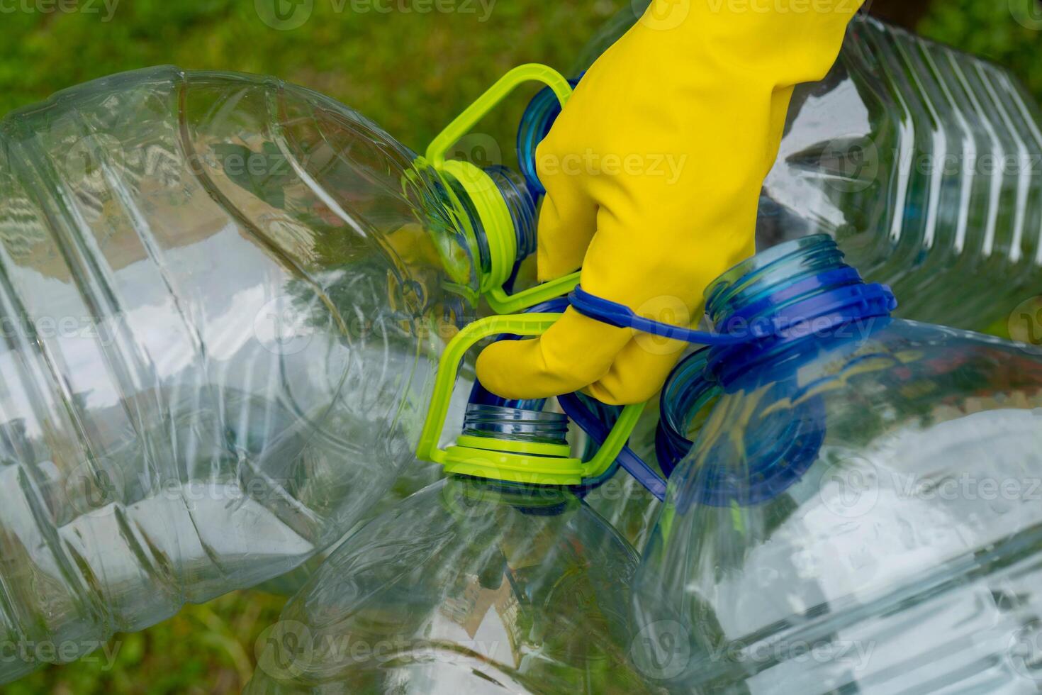 Garbage collection. Hand in yellow glove holding big empty plastic bottles. Grass on a background. photo