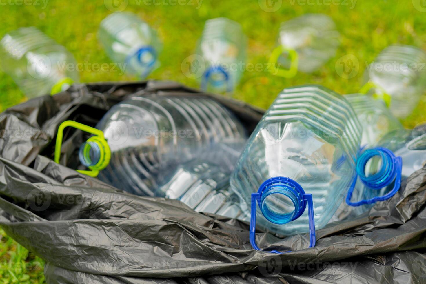 Plastic bottles in a black plastic trash bag on a grass background. photo
