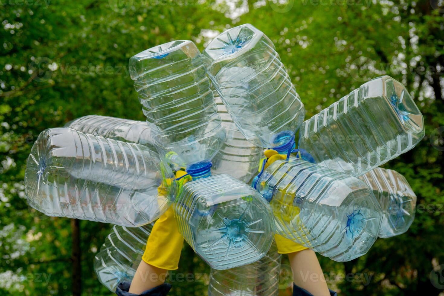 Garbage collection. Hands in yellow gloves holding big empty plastic bottles. Grass on a background. photo