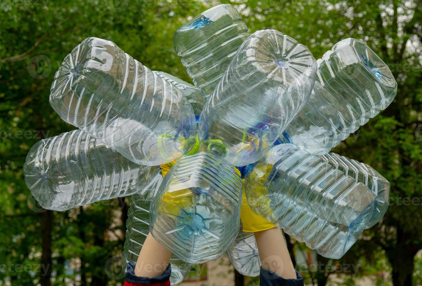 Garbage collection. Hands in yellow gloves holding big empty plastic bottles. Grass on a background. photo