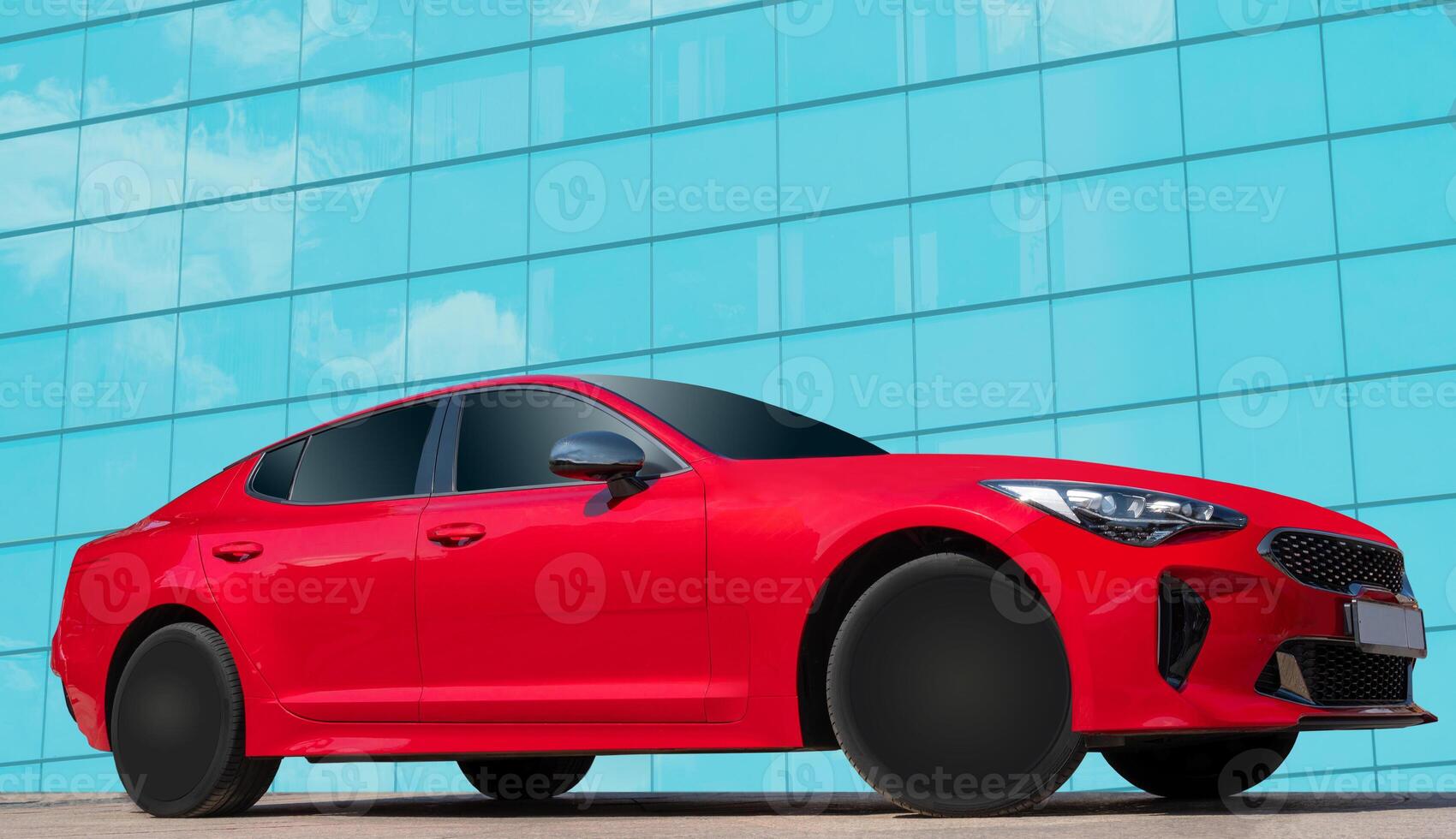 Red car on a background of a mirrored wall of a house with clouds reflections. Stylish, modern, bright image of the car for design solutions. photo
