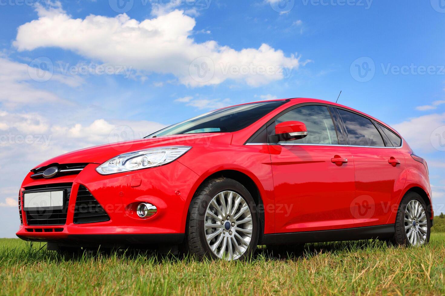 Red car on a blue sky background with white clouds. The car is standing in the field on the green grass. photo