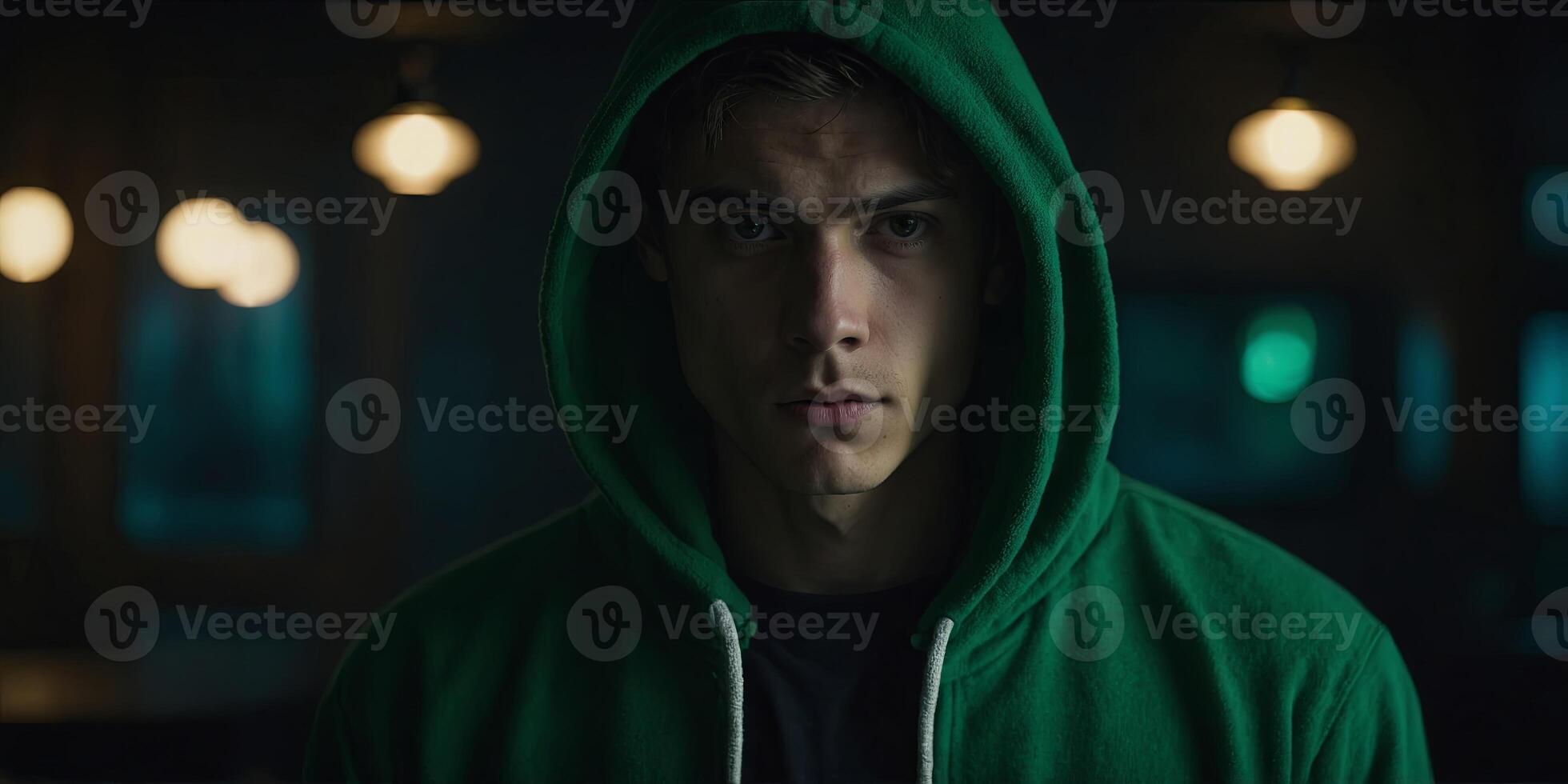 A young man with a green hoodie and black shirt is standing in a dark room. photo