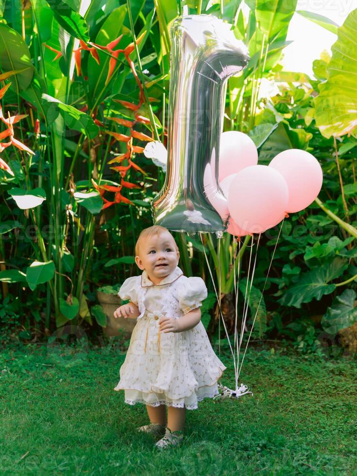 One year birthday of baby girl with air balloons in garden. Charming little child in dress. photo