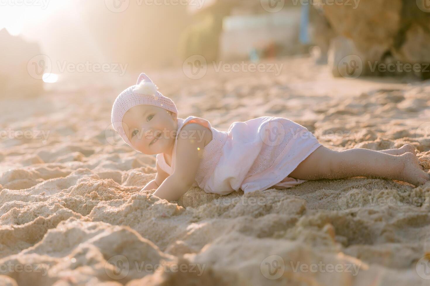 Baby girl in pink dress play on ocean beach with sunset light. photo