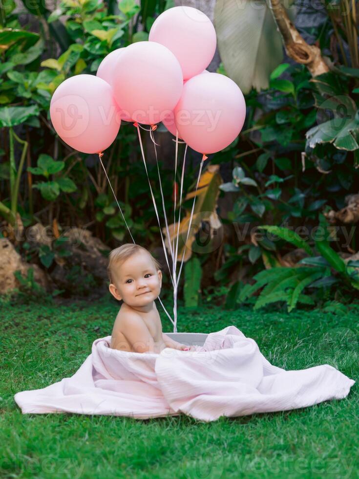 Baby girl with air balloons sit in baby bath outdoor garden. Happy baby. photo