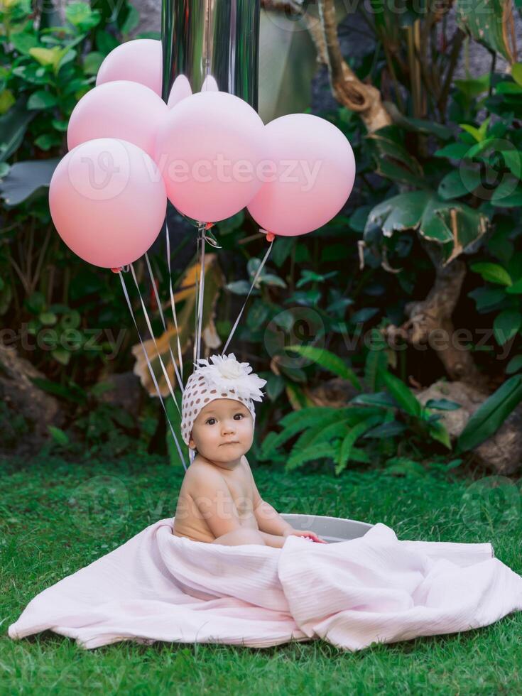 Happy baby girl and air balloons swim in baby bath outdoor garden. photo