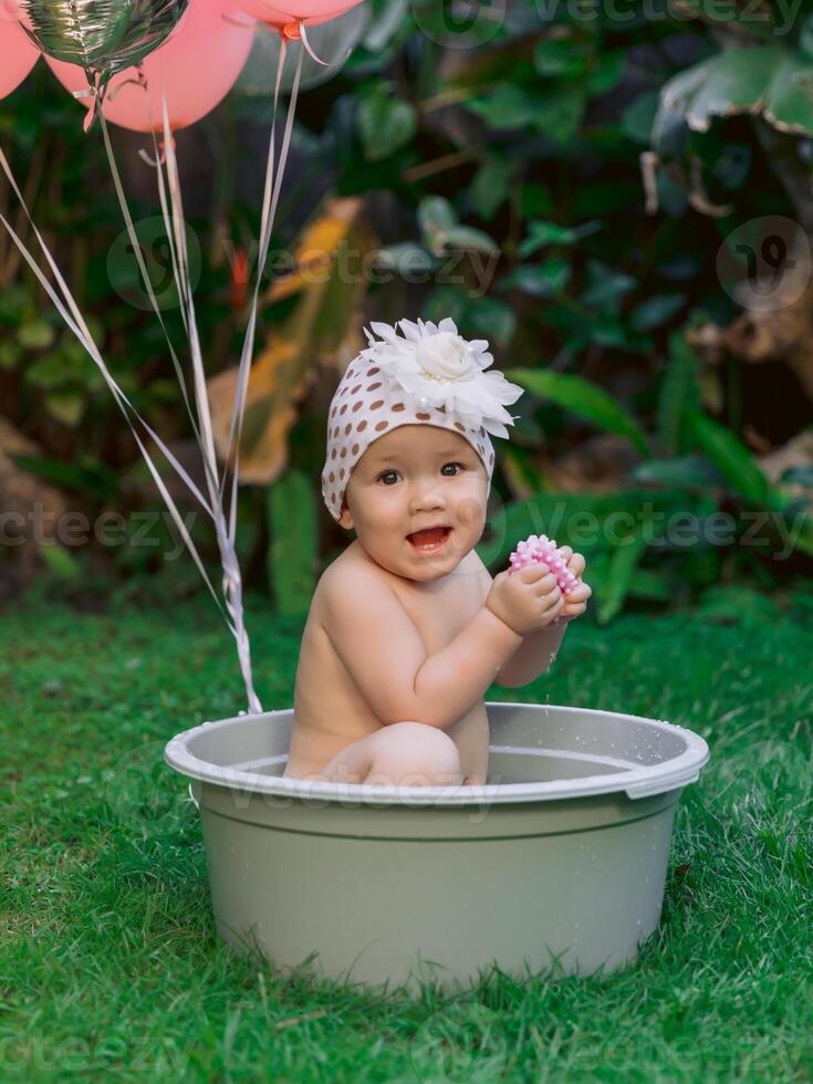 Happy child girl and pink air balloons swimming in baby bath outdoor summer garden. photo