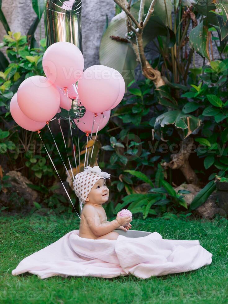 Baby girl and pink air balloons swim in baby bath outdoor garden. Happy baby. photo