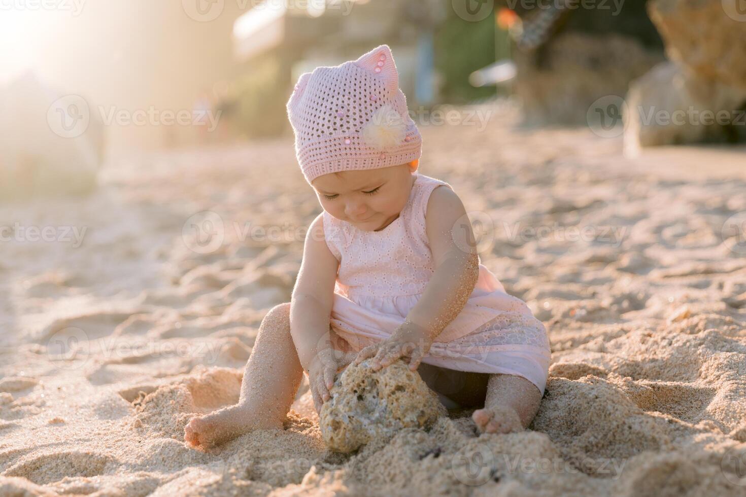 Baby girl in pink dress playing on sandy beach with sunshine photo